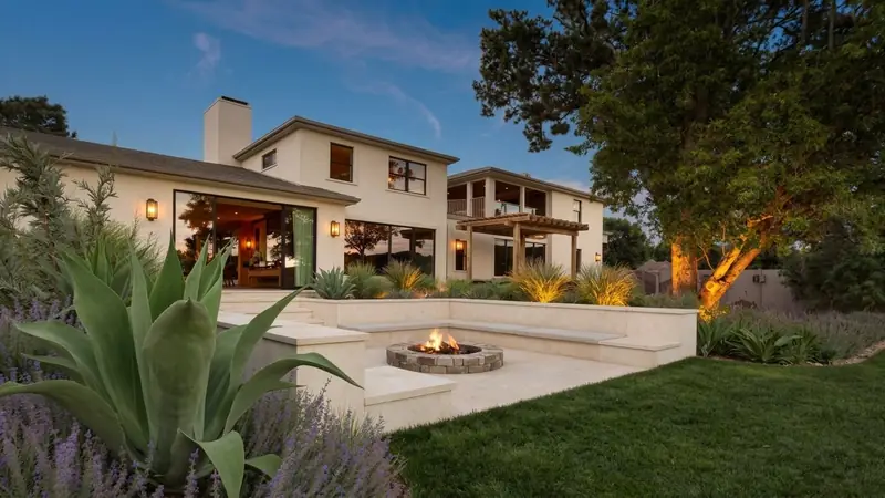 A limestone patio and fire pit at dusk, lit by warm landscape lighting